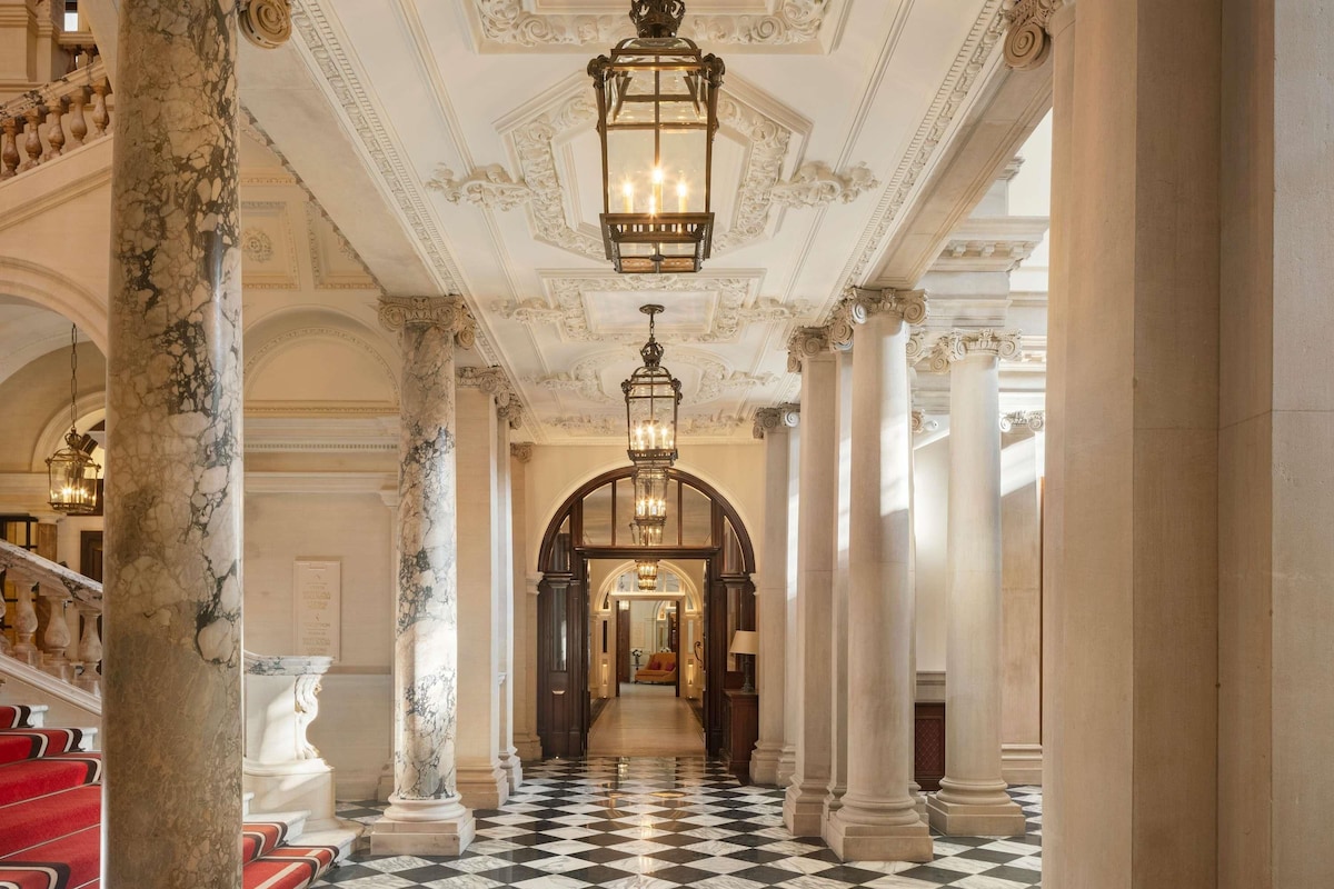 A grand hallway with marble columns, a checkered floor, and a staircase with red steps.