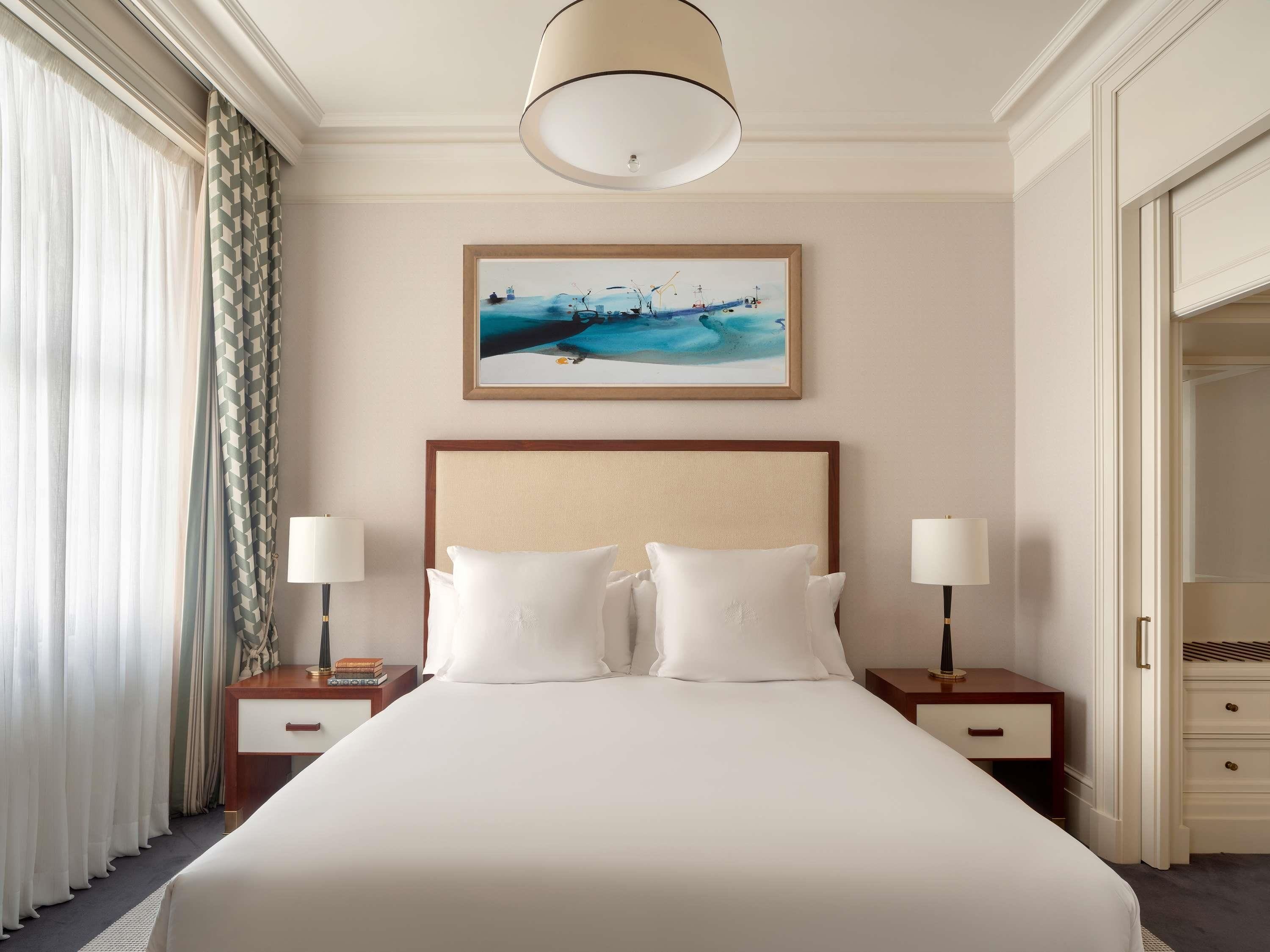 Een hotelkamer met een groot bed, twee nachtkastjes met lampen, een schilderij aan de muur en een kledingkast.