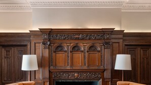 A room with a fireplace, two armchairs, a rug, and a wooden mantelpiece. - Raffles London at The OWO (London)