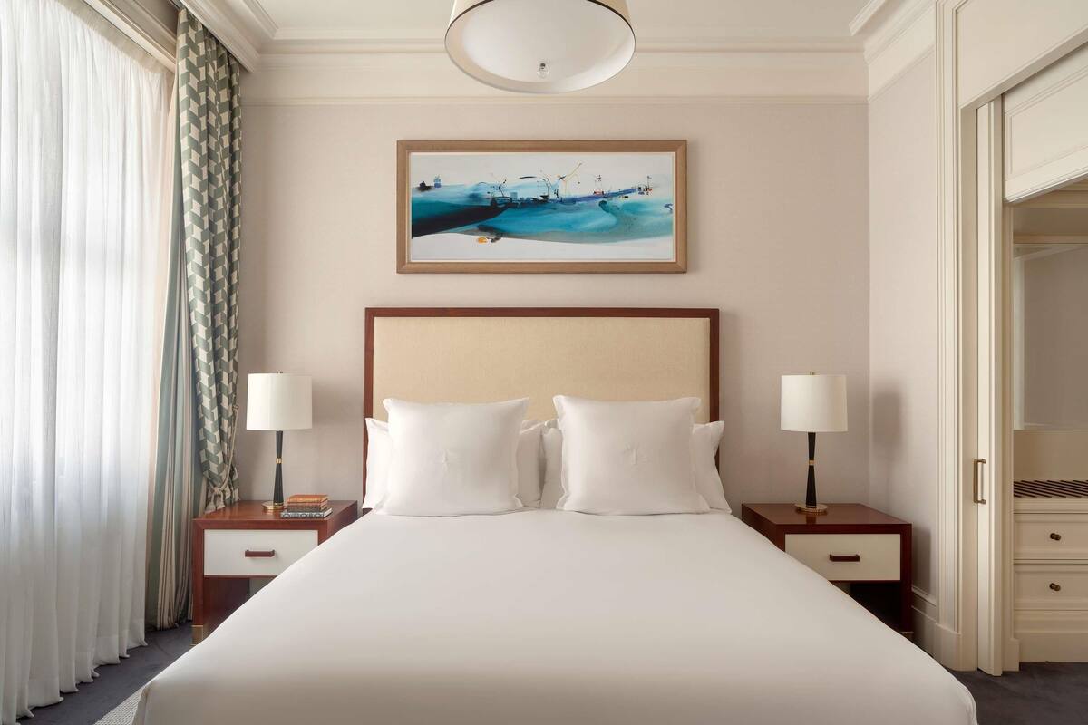 A hotel room with a large bed, two bedside tables with lamps, a painting on the wall, and a closet.