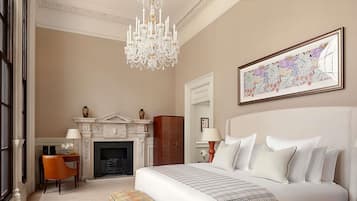 A hotel room with a large bed, a bench, a fireplace, a chandelier, and a framed floral artwork.