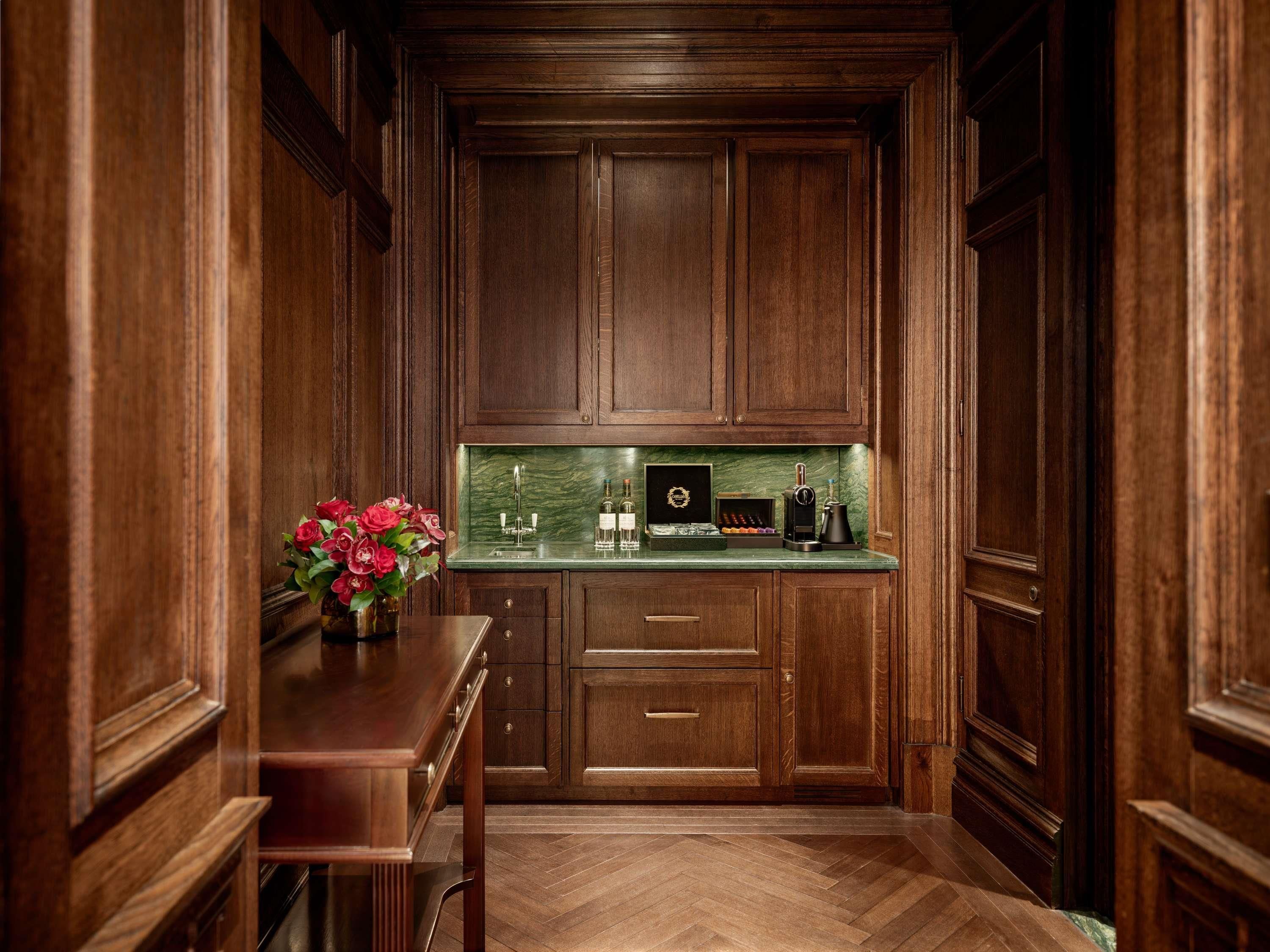 A kitchen with wooden cabinets, a marble countertop, a coffee machine, and a vase with flowers.