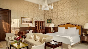 Habitación de hotel con una cama grande, un sofá, una mesita con un jarrón de flores, un armario de madera y un candelabro.