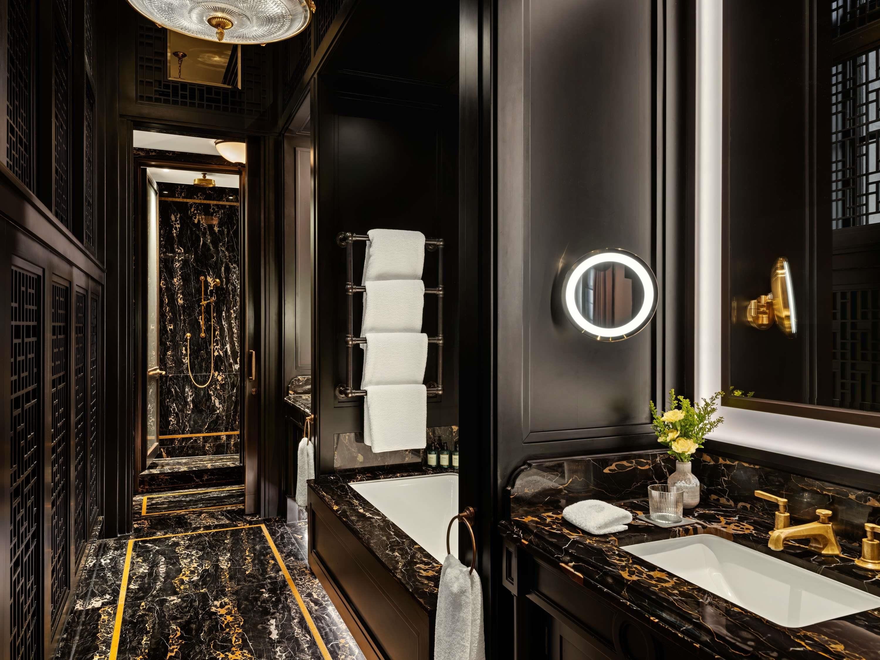 A modern bathroom with a marble floor, a large mirror, a bathtub, and a vanity with a sink.