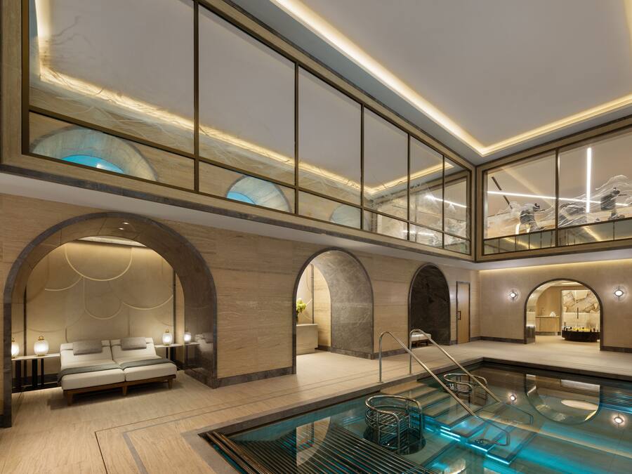 A modern hotel lobby with a pool, arched doorways, and a seating area.