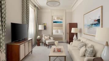 A hotel room with a flat-screen TV, a sofa, a coffee table, a cabinet, a lamp, and a painting on the wall.