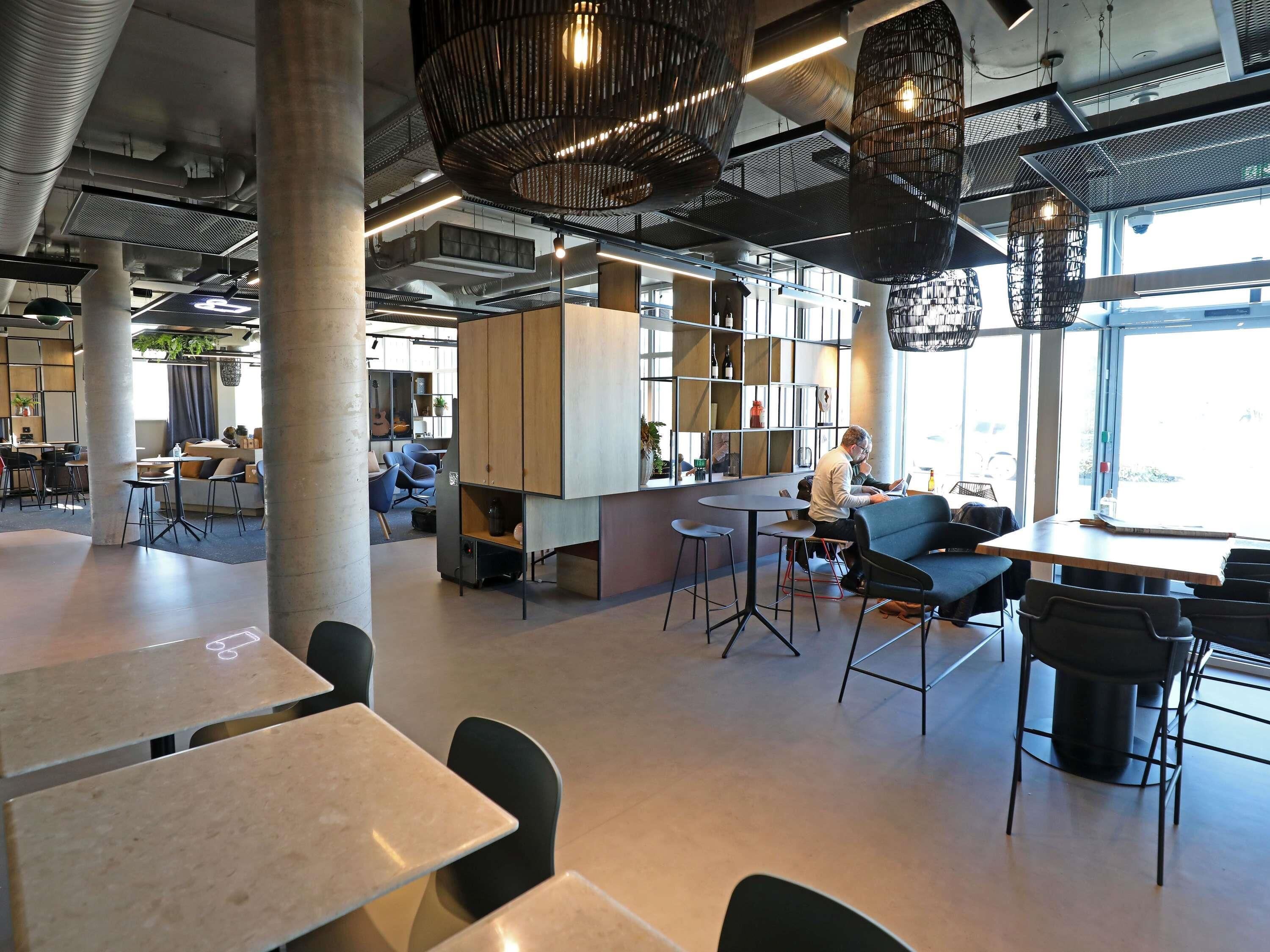 Een modern interieur met hoge plafonds, blootgelegde leidingen en industriële verlichtingsarmaturen.