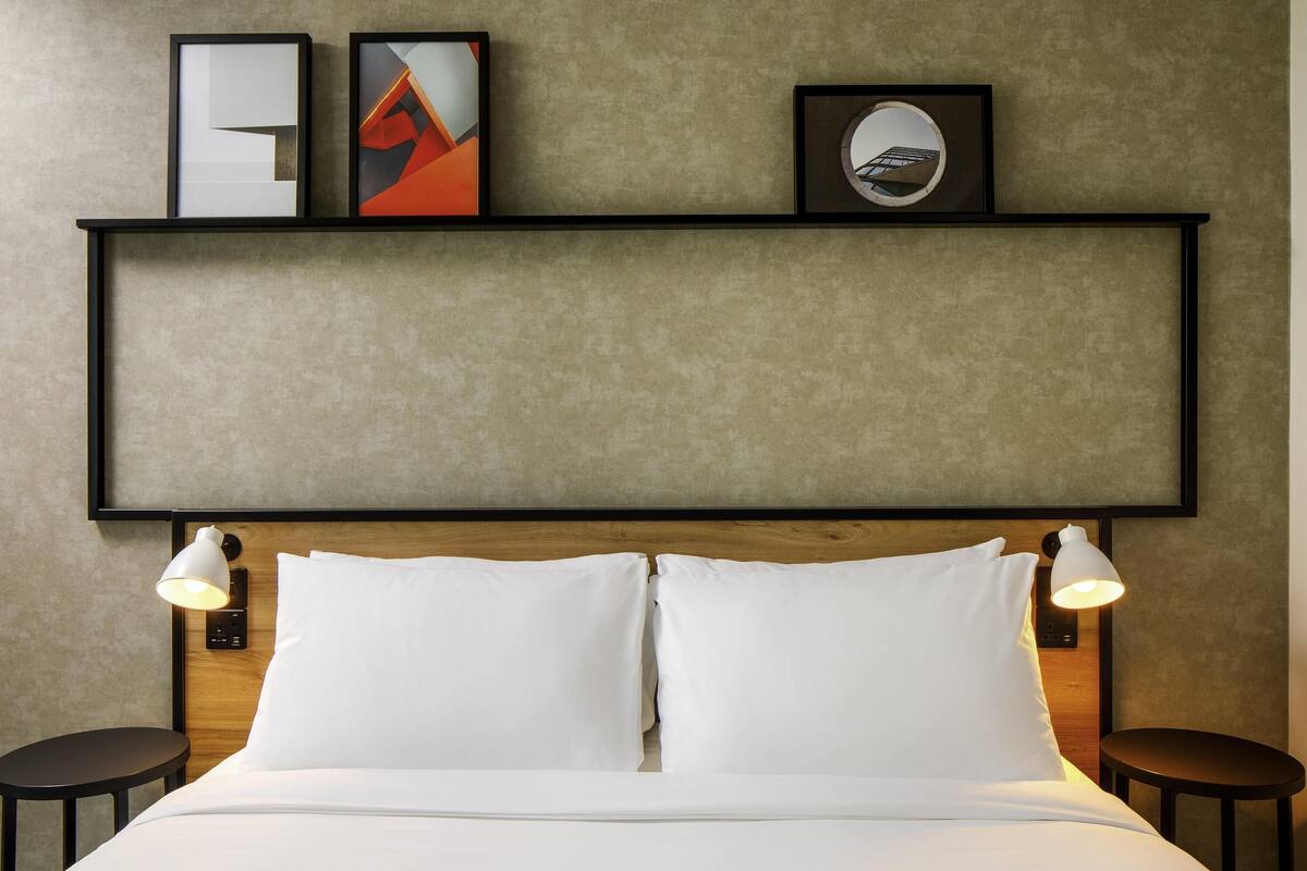 A hotel room with a bed, two bedside tables, a headboard, and wall-mounted artwork.