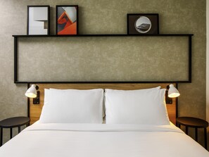 A hotel room with a bed, two bedside tables, a headboard, and wall-mounted artwork.