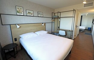 Habitación de hotel con una cama grande, un escritorio y una silla. Hay tres cuadros enmarcados en la pared sobre la cama.
