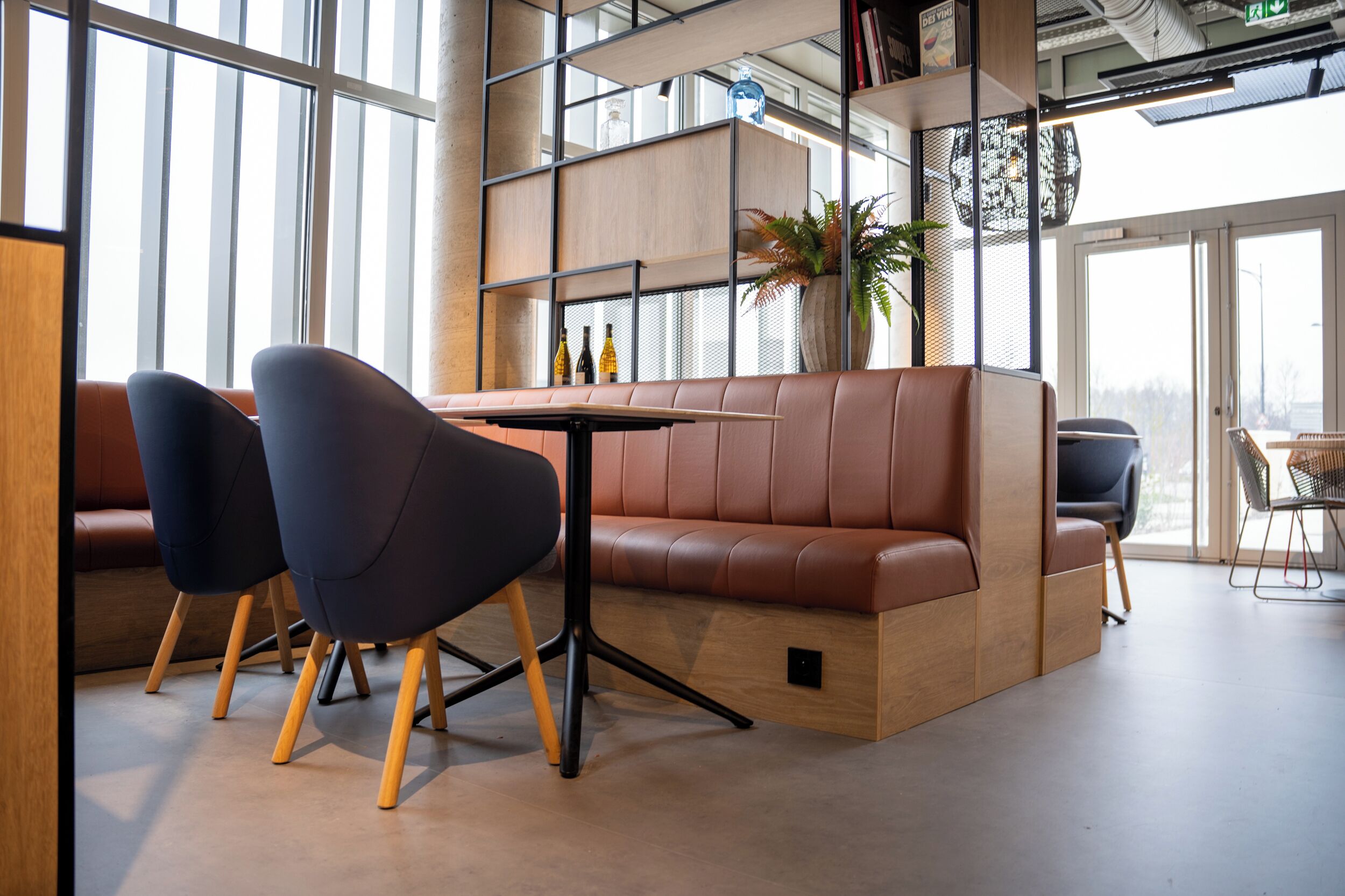 A modern interior with a brown leather sofa, two dark chairs, a wooden table, and a large window.
