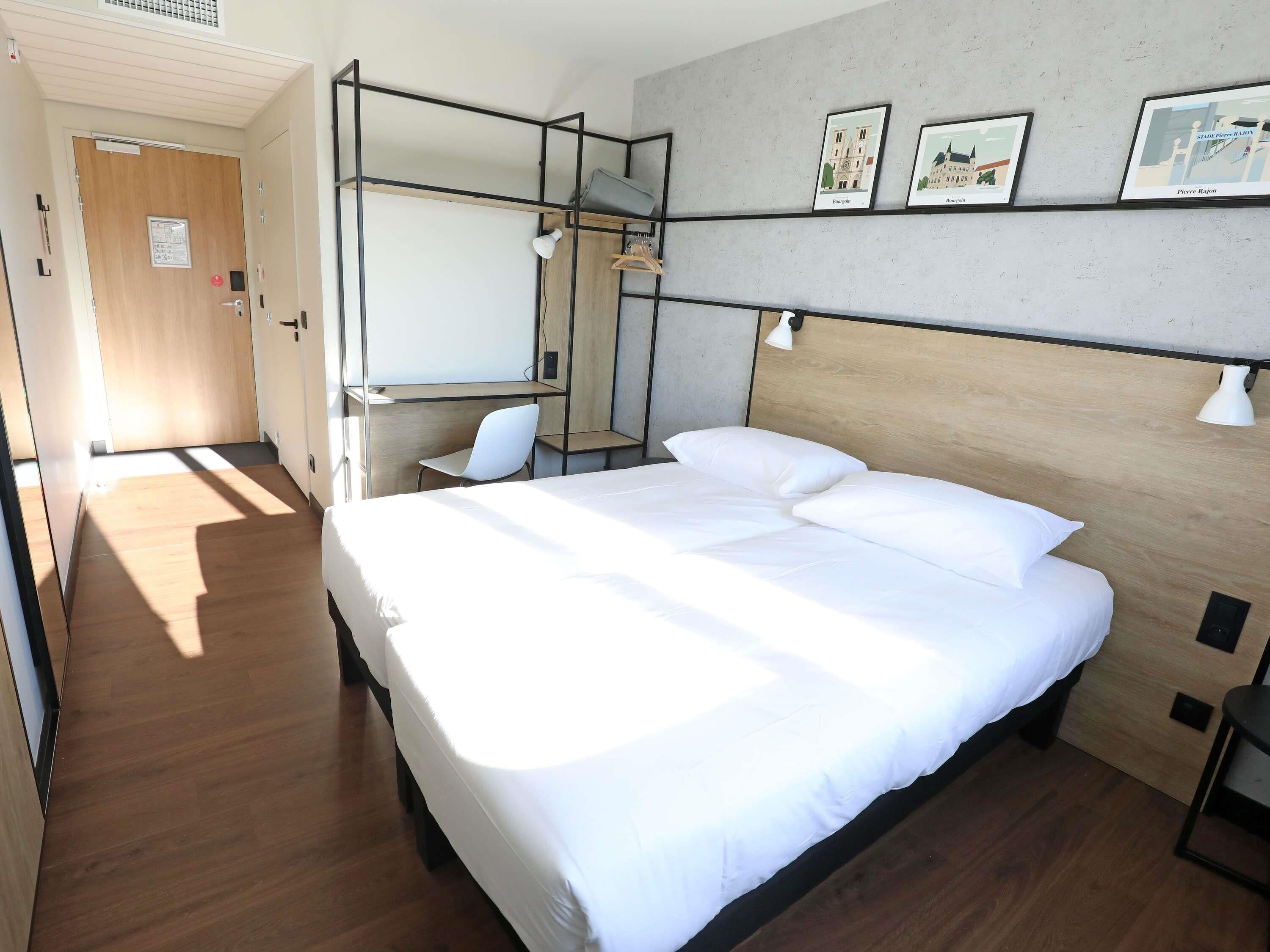 Ein Hotelzimmer mit einem Bett, einem Schreibtisch und einem Sessel. An der Wand befinden sich Wandleuchten und gerahmte Bilder.
