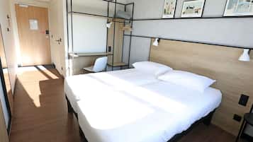 Ein Hotelzimmer mit einem Bett, einem Schreibtisch und einem Sessel. An der Wand befinden sich Wandleuchten und gerahmte Bilder.