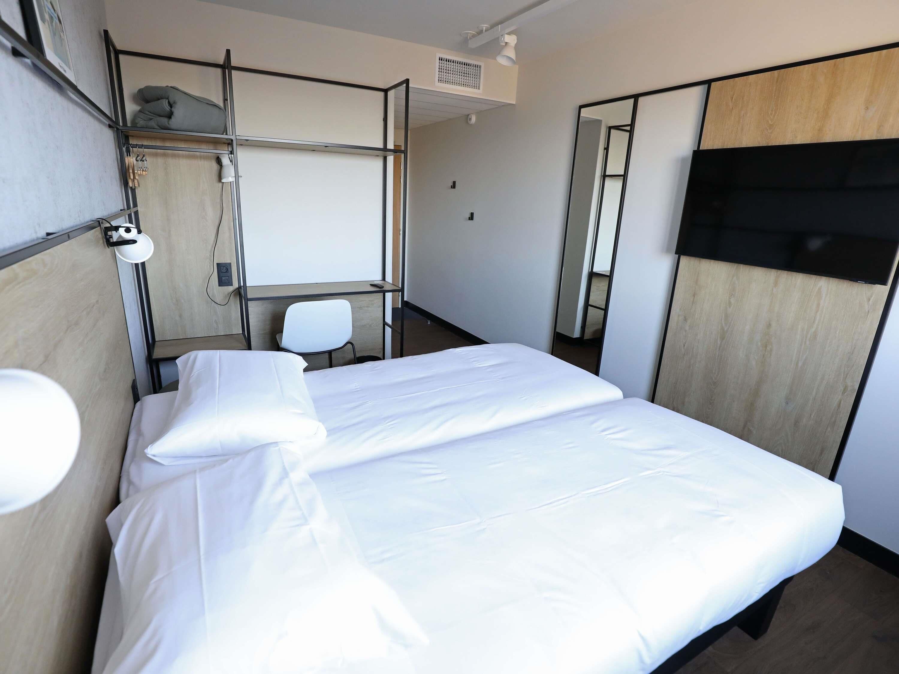 Hotellihuone, jossa on sänky, työpöytä, tuoli, peili ja vaatekaappi.