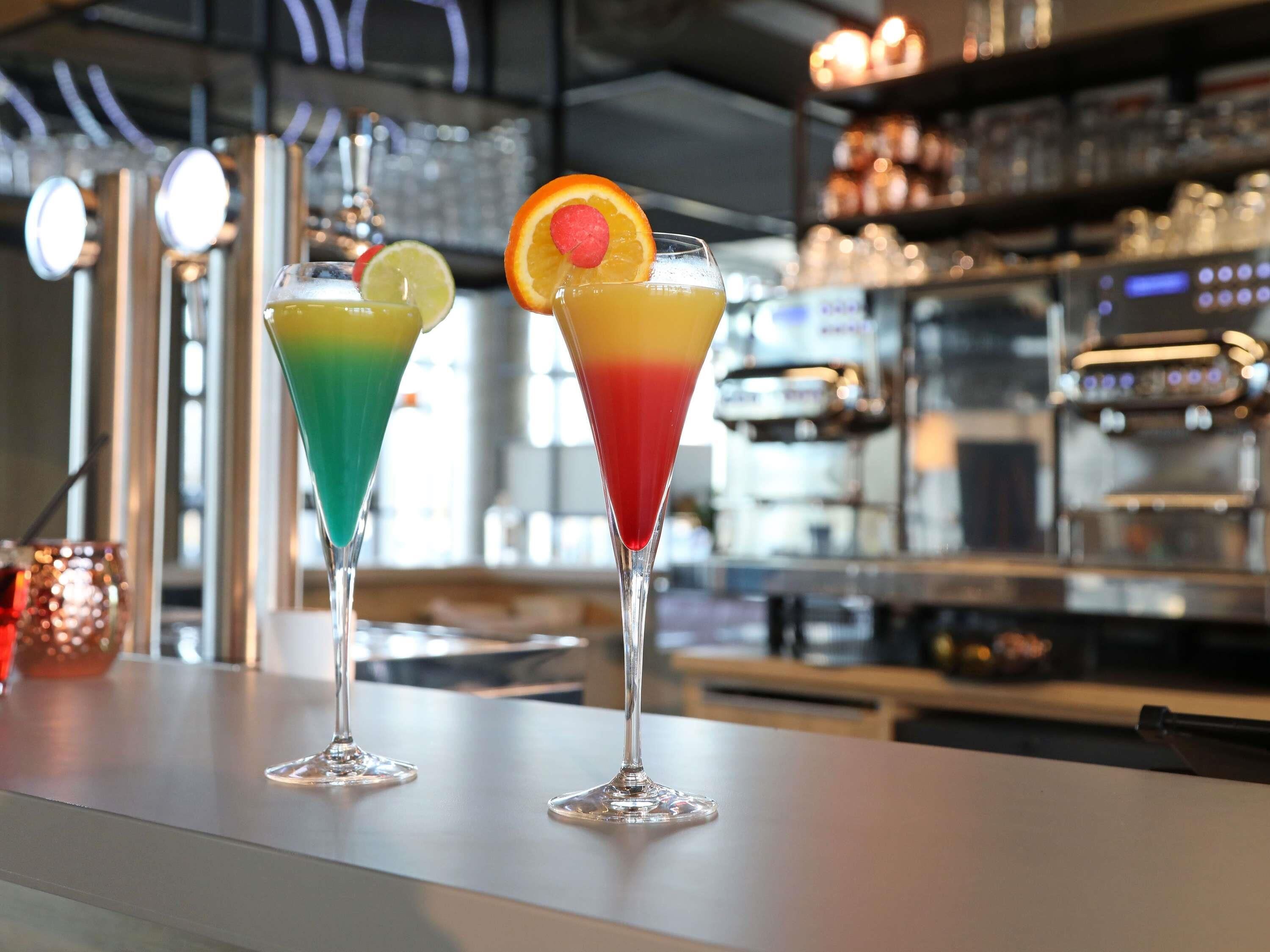 Two colorful cocktails on a bar counter with a blurred background of a bar area.