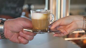 Una persona sosteniendo una taza de vidrio con una bebida, probablemente café, y una cuchara en su interior.