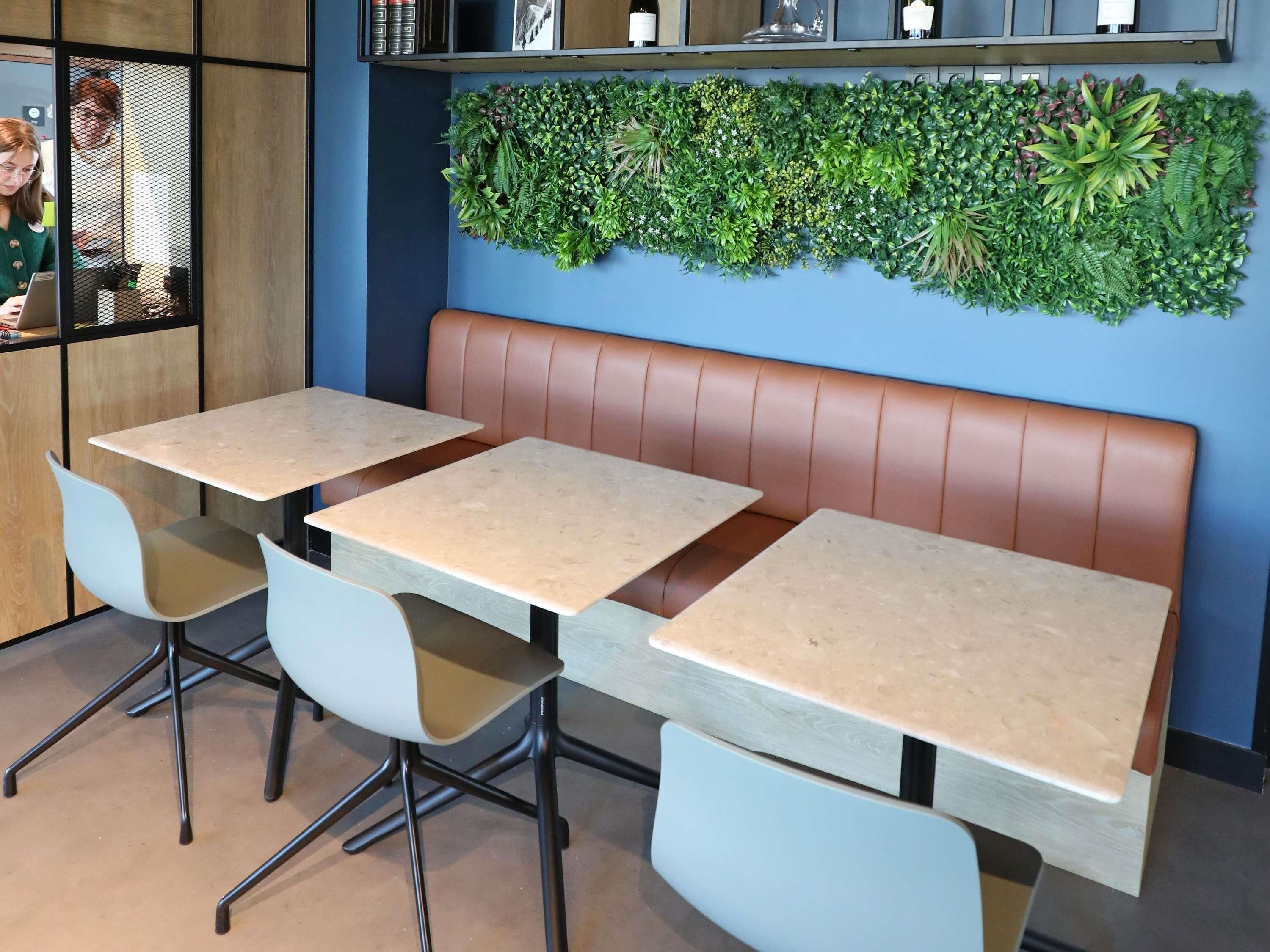A restaurant interior with a booth seating area, tables, chairs, and a green wall decoration.