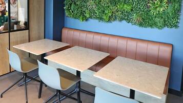A restaurant interior with a booth seating area, tables, chairs, and a green wall decoration.