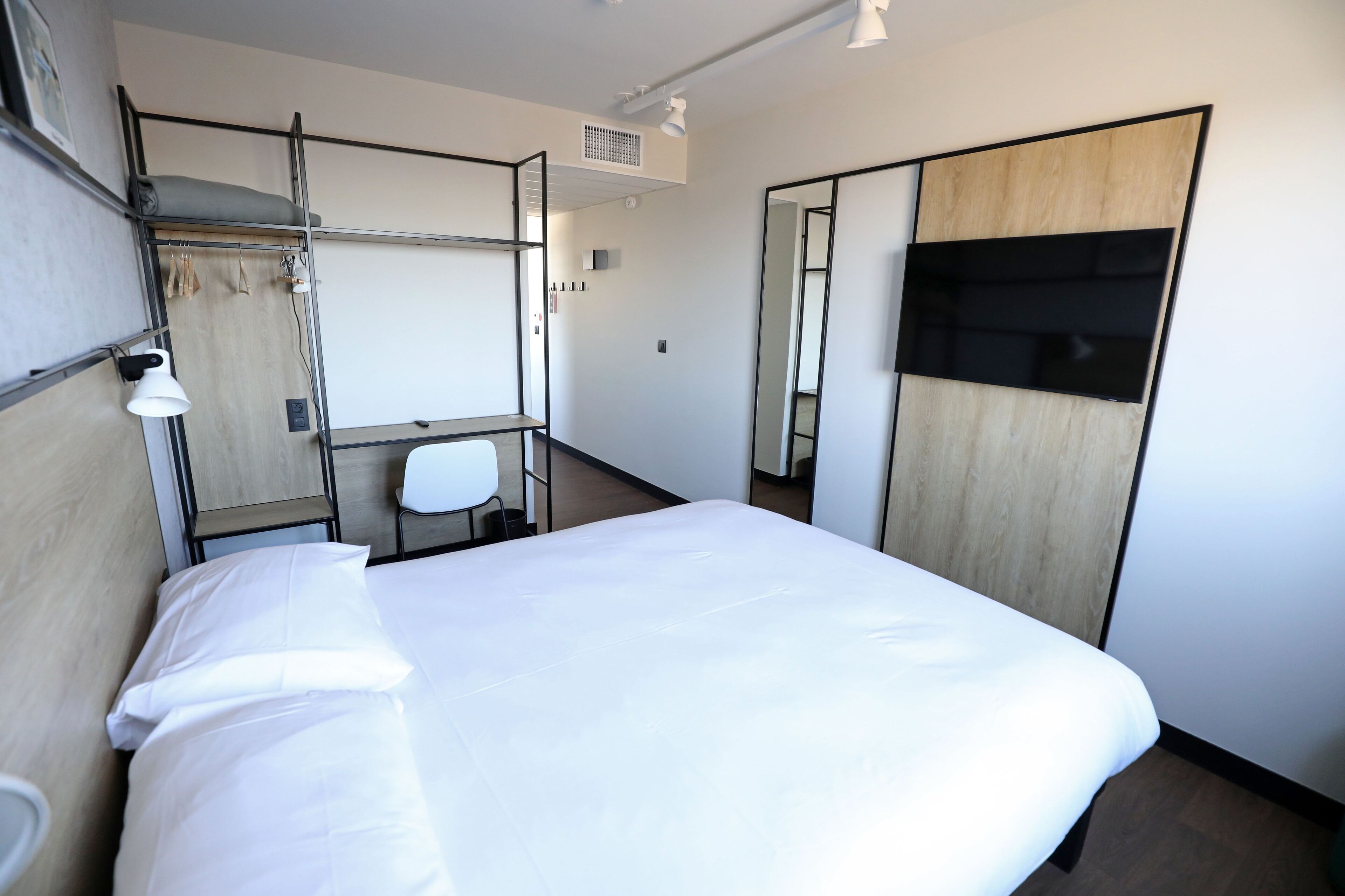 Une chambre d’hôtel comprenant un lit, un bureau, une chaise, une armoire et un miroir.