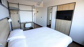 Une chambre d’hôtel comprenant un lit, un bureau, une chaise, une armoire et un miroir.