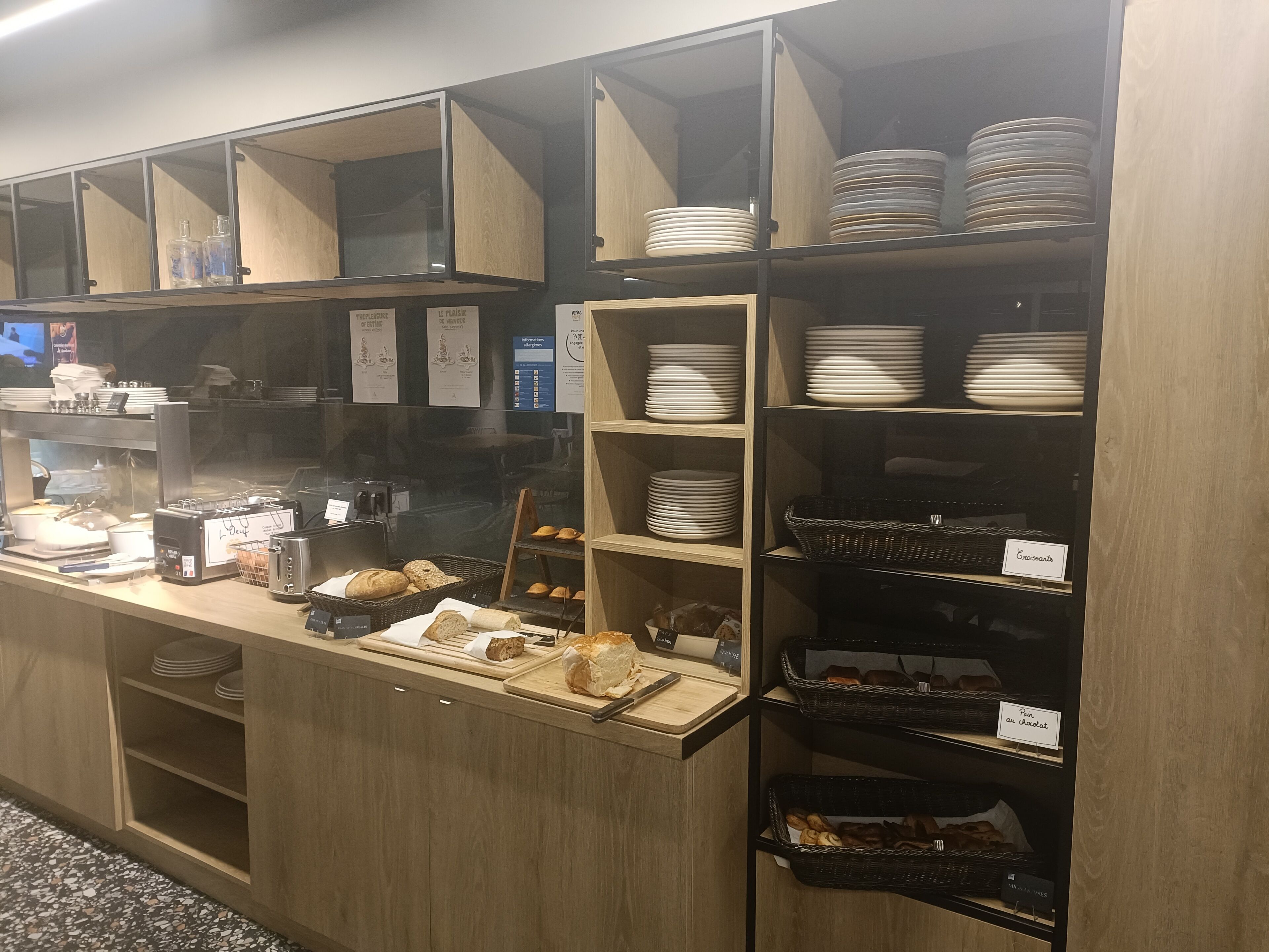 Une vitrine de boulangerie avec du pain et des pâtisseries, une machine à café, ainsi que différentes assiettes et bols.