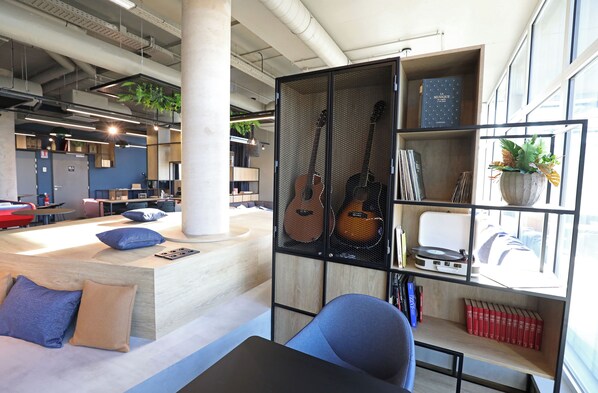 A modern workspace with a desk, chairs, and a shelving unit with guitars and books.