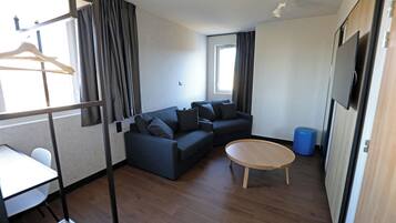 Ein modernes Wohnzimmer mit einem Ecksofa, einem runden Couchtisch aus Holz und einem an der Wand montierten Fernseher.