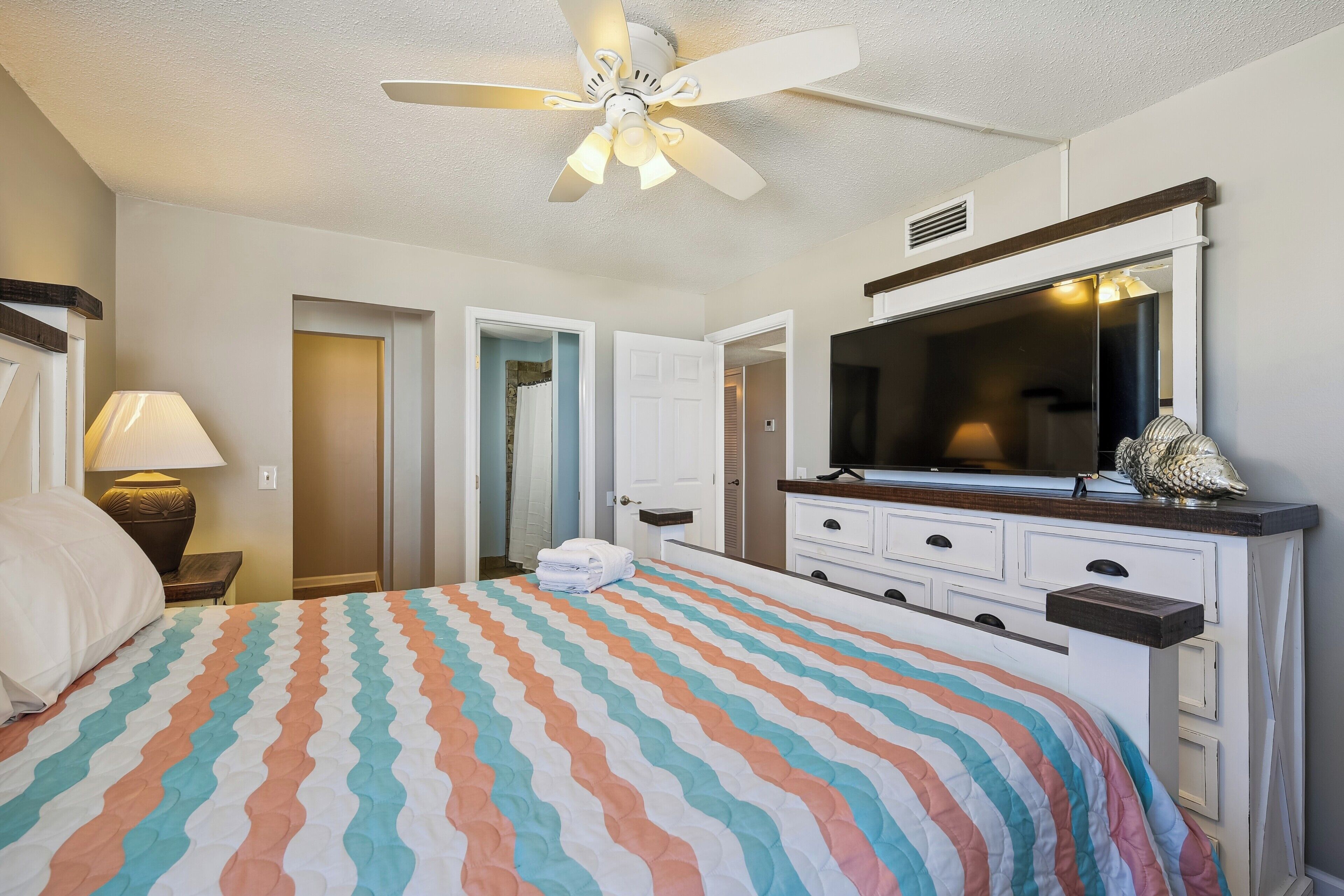 A hotel room with a bed, a ceiling fan, a TV, and a dresser.
