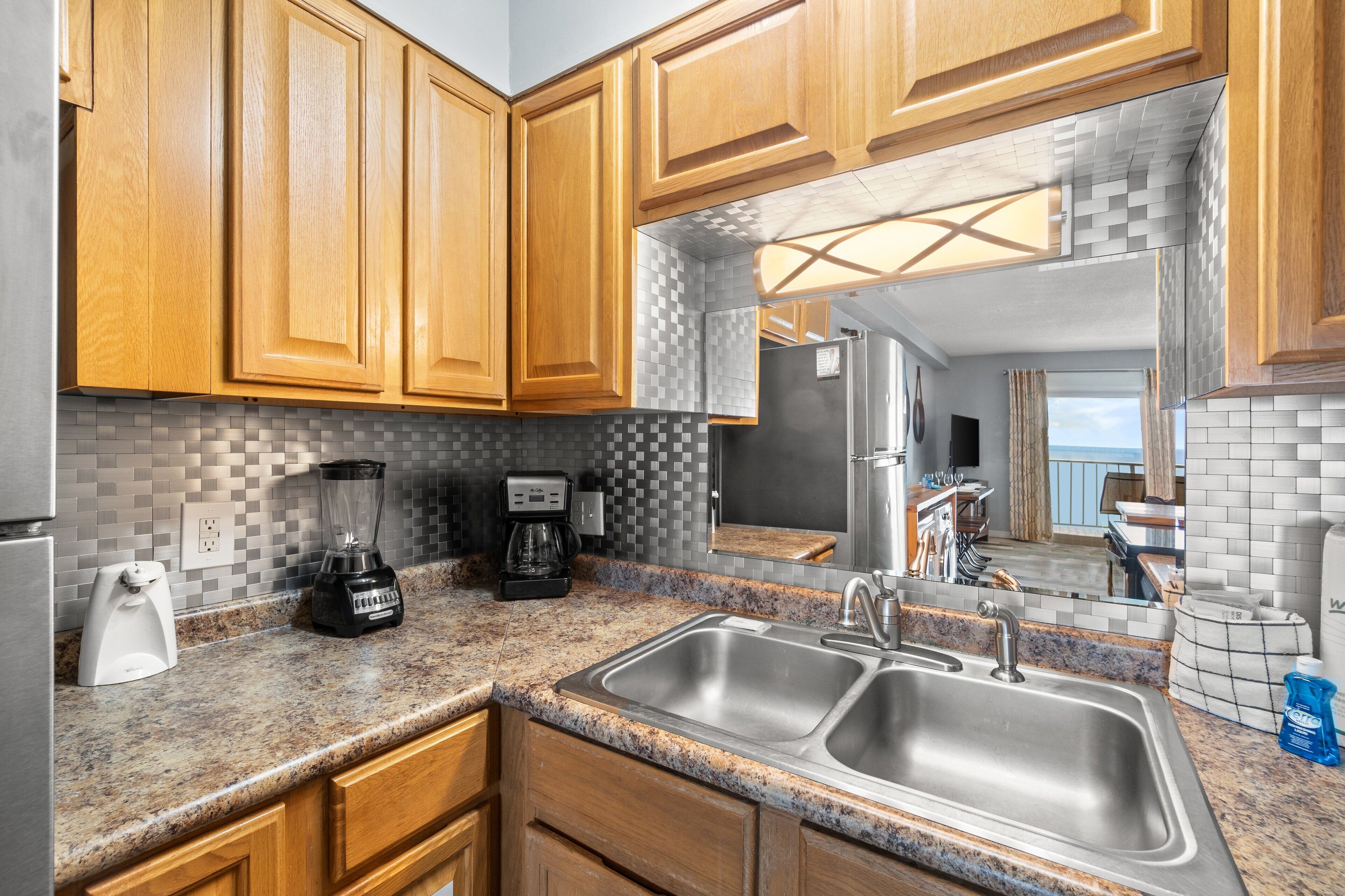 A kitchen with wooden cabinets, granite countertops, a double sink, a coffee maker, and a blender.