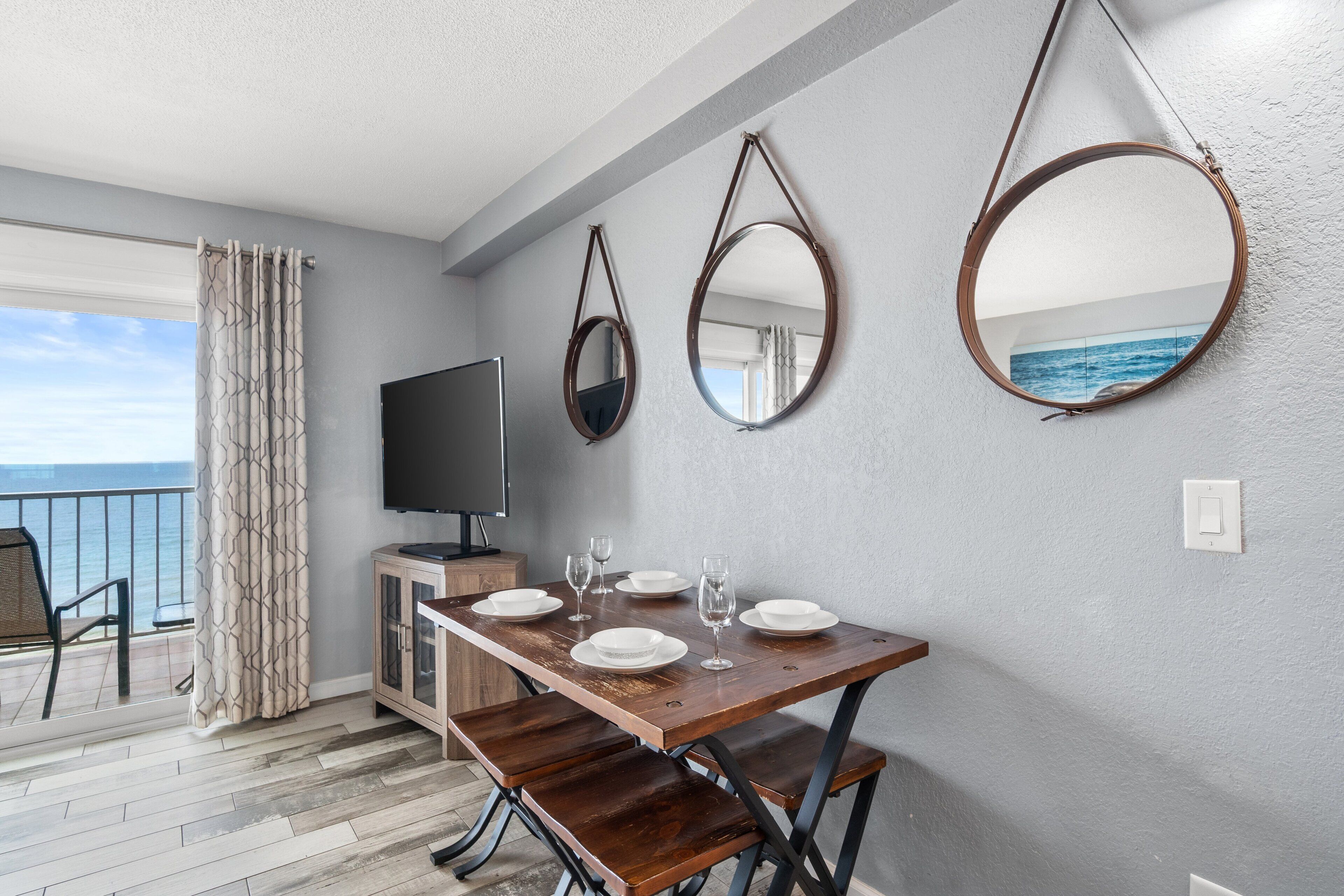 A dining area with a wooden table set for four, a television on a cabinet, and three wall-mounted mirrors.