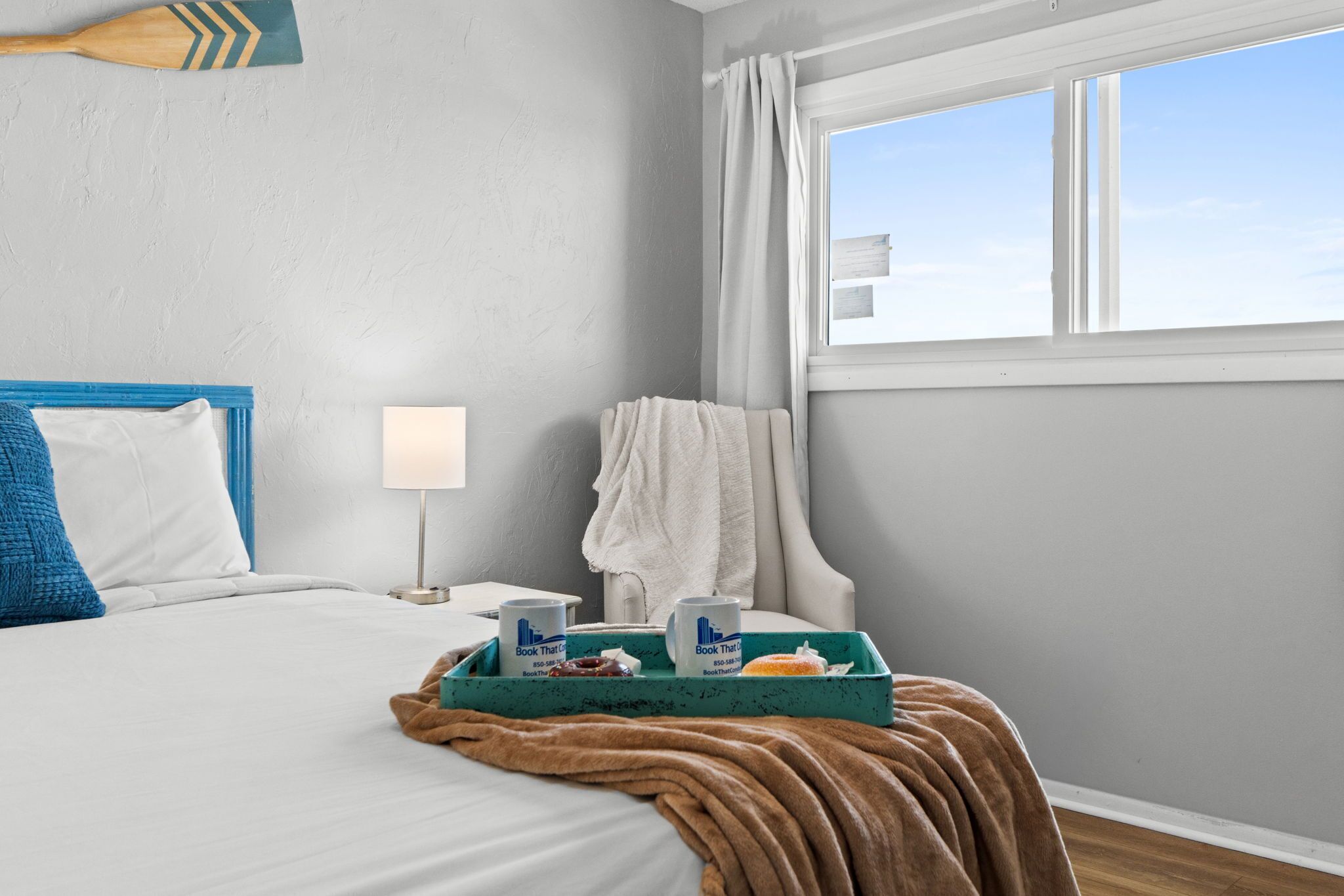 A hotel room with a bed, a nightstand, a window with curtains, and a tray with breakfast items.