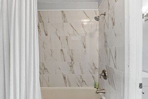 A bathroom with marble tiles, a shower, and a bathtub.