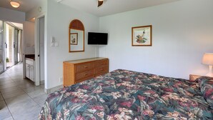 Un dormitorio con cama, cómoda, ventilador de techo, televisor de pantalla plana y puerta que da al baño.