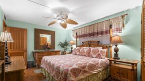 Un dormitorio con cama, mesitas de noche, ventilador de techo, espejo y ventana con cortinas.