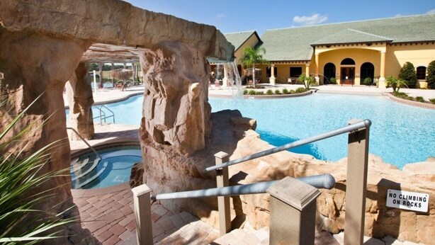 Zona de piscina con una formación rocosa y un cartel que prohíbe escalar las rocas.