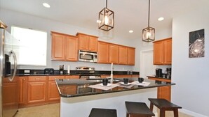 Una cocina moderna con armarios de madera, una isla central con taburetes, electrodomésticos de acero inoxidable e iluminación colgante.