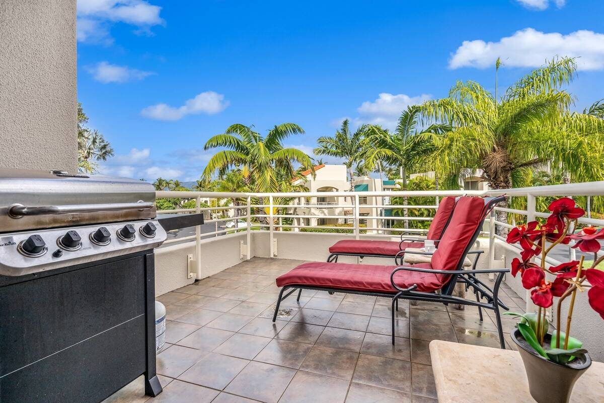 An outdoor patio with a grill, red lounge chairs, and potted red orchids.