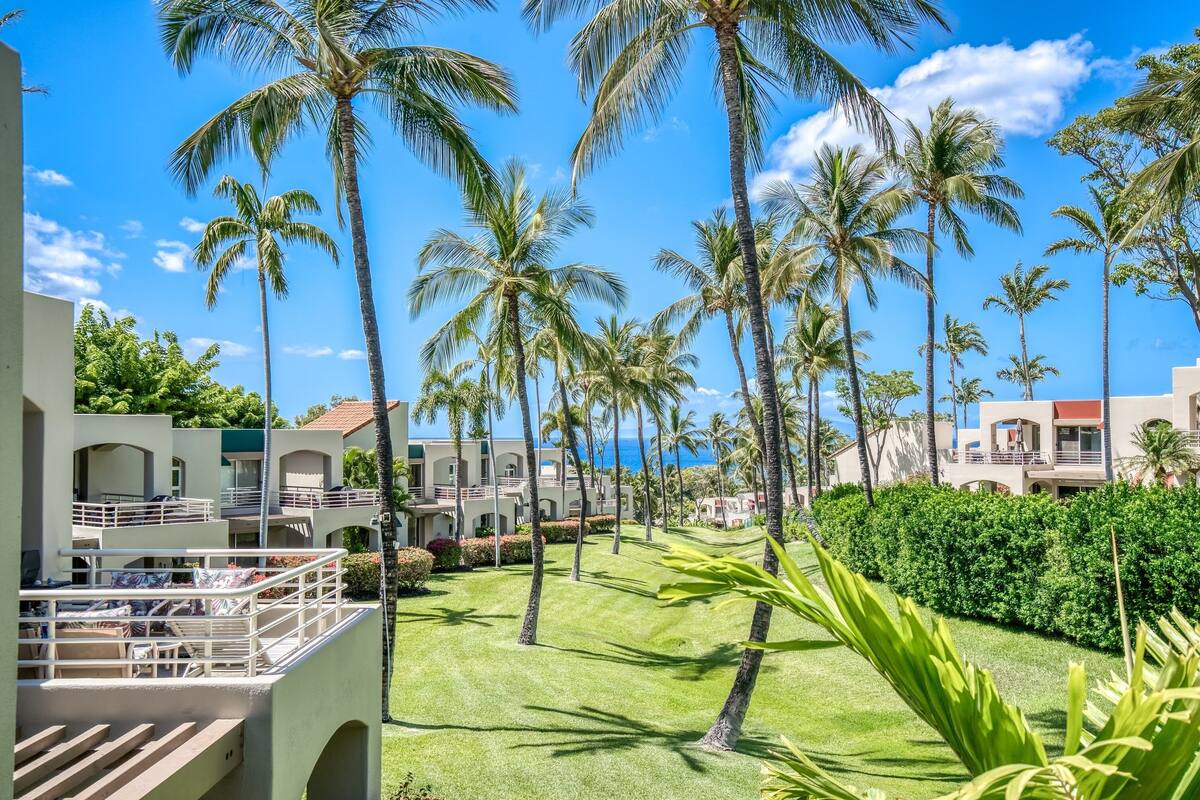 A resort with multiple-story buildings, palm trees, and a well-maintained lawn.