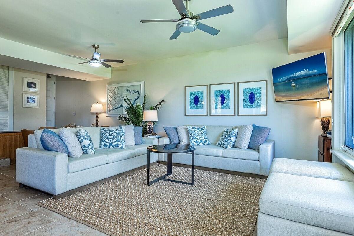 A living room with a sectional sofa, a coffee table, a ceiling fan, and artwork on the walls.