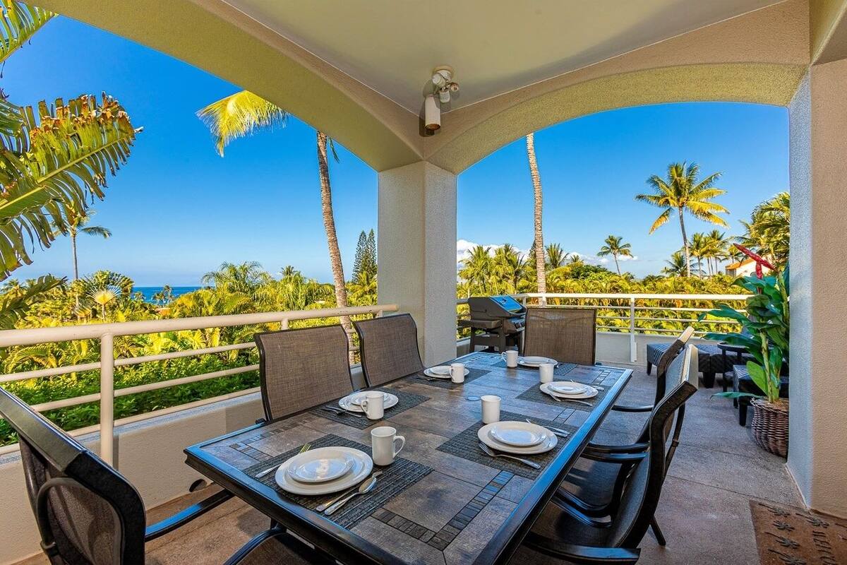 A dining area with a table set for four, overlooking a scenic view of palm trees and the ocean.