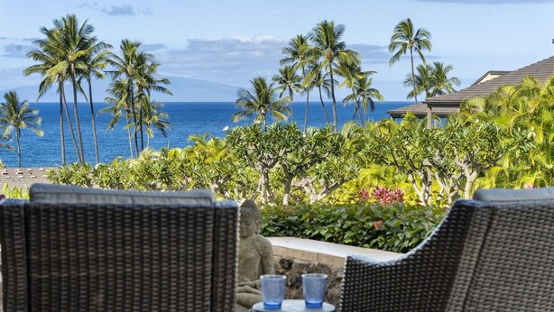 A view of a beachside resort with wicker chairs and a table, palm trees, and the ocean in the background. - Wailea Elua by Coldwell Banker Island Vacations (Kihei)