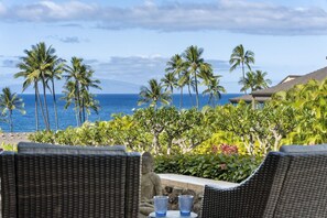 A view of a beachside resort with wicker chairs and a table, palm trees, and the ocean in the background. - Wailea Elua by Coldwell Banker Island Vacations (Kihei)