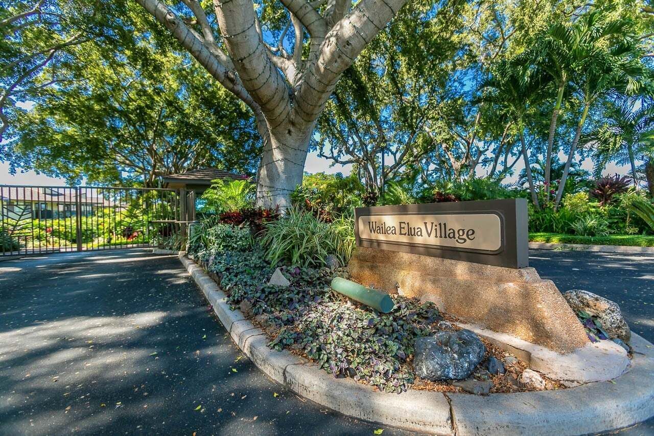 A sign for Wailea Elua Village with a landscaped area featuring a tree and plants.