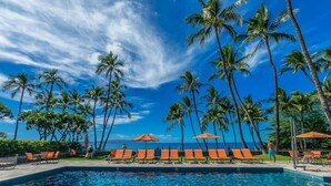 A poolside area with lounge chairs and umbrellas, surrounded by palm trees and a clear blue sky. - Wailea Elua by Coldwell Banker Island Vacations (Kihei)