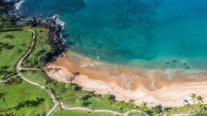 An aerial view of a beach with clear turquoise waters, a sandy shore, and a golf course with palm trees. - Wailea Elua by Coldwell Banker Island Vacations (Kihei)