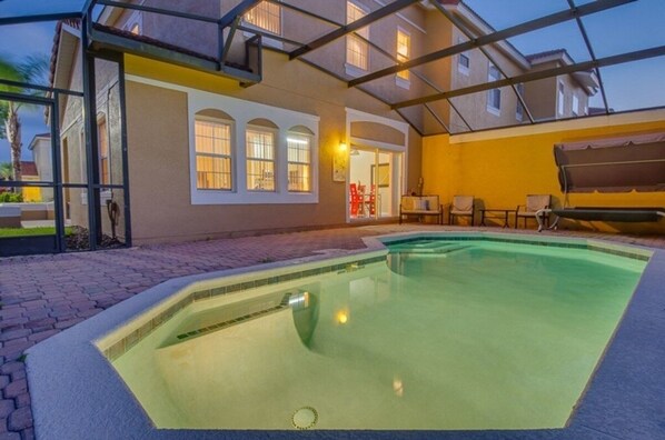 Una piscina con zona cubierta, un patio con sillas y un edificio con ventanas de arco.