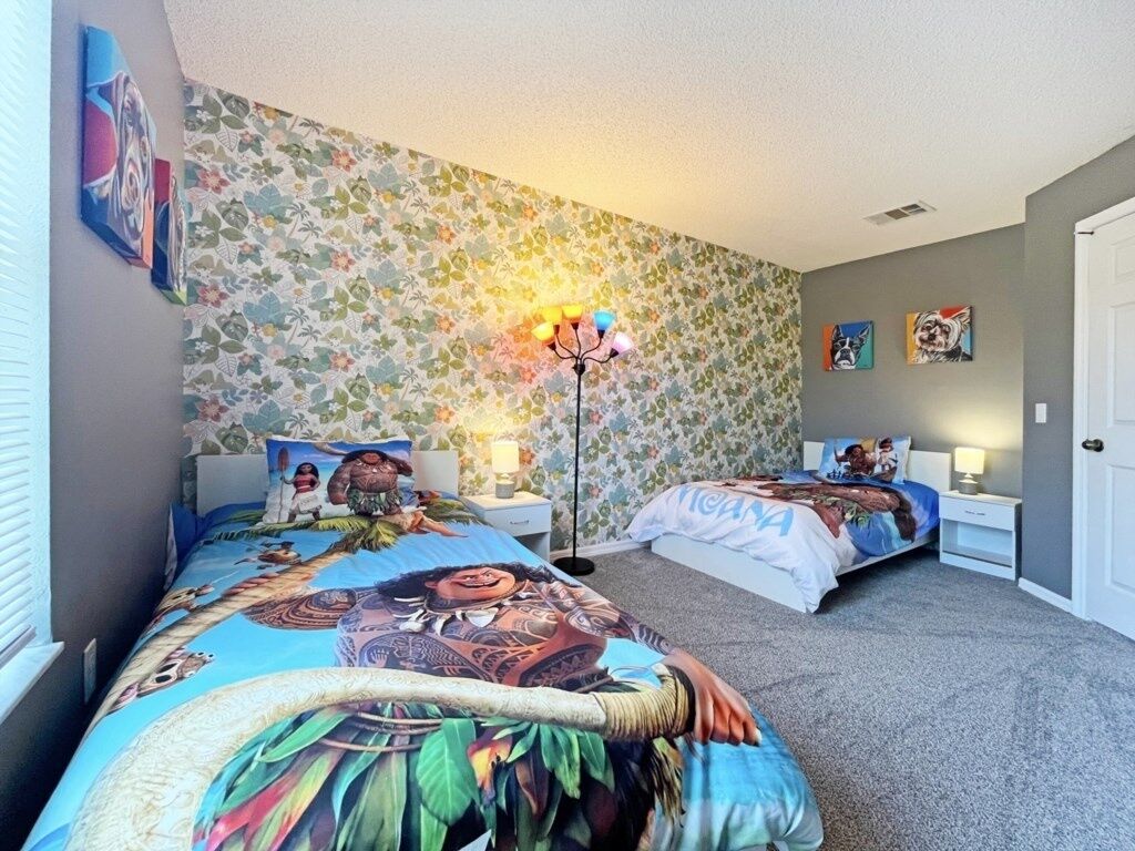 Een slaapkamer met twee bedden, bloemenbehang en kunstwerken aan de wanden.