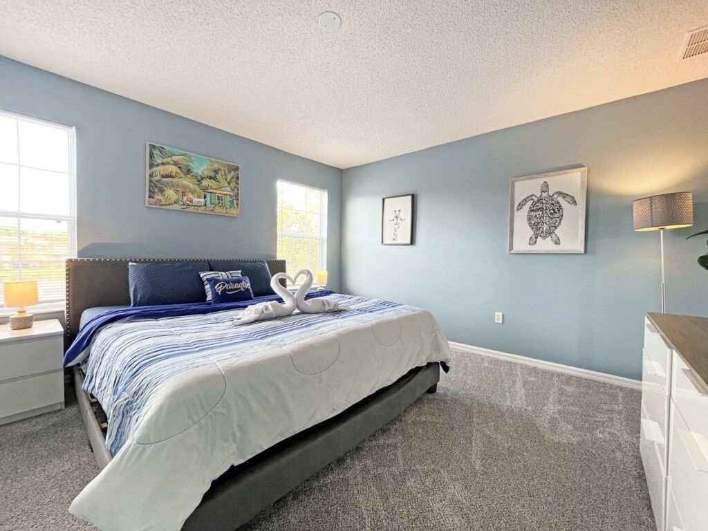 A bedroom with a bed, a nightstand, a dresser, and wall art.