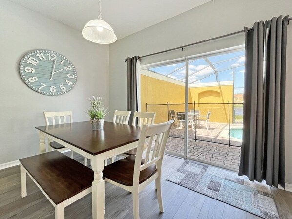 Un comedor con mesa y sillas, un reloj en la pared y vistas a un patio exterior con piscina.