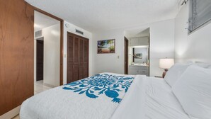 A hotel room with a bed, a wooden wardrobe, a door, a painting, a mirror, and a window. - Big Island Kona Ali'i by Coldwell Banker Island Vacations (Kailua-Kona)